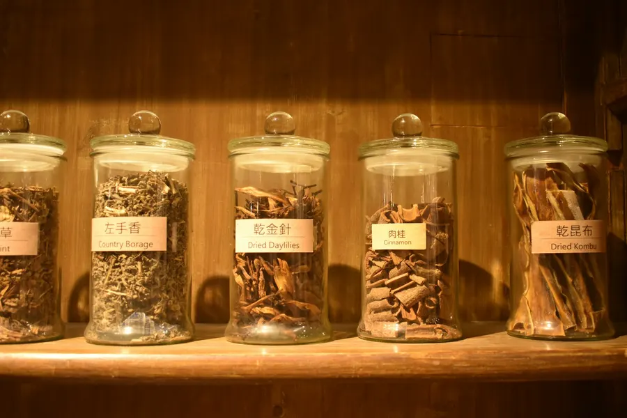 A shelf of labeled glass jars holding dried herbs